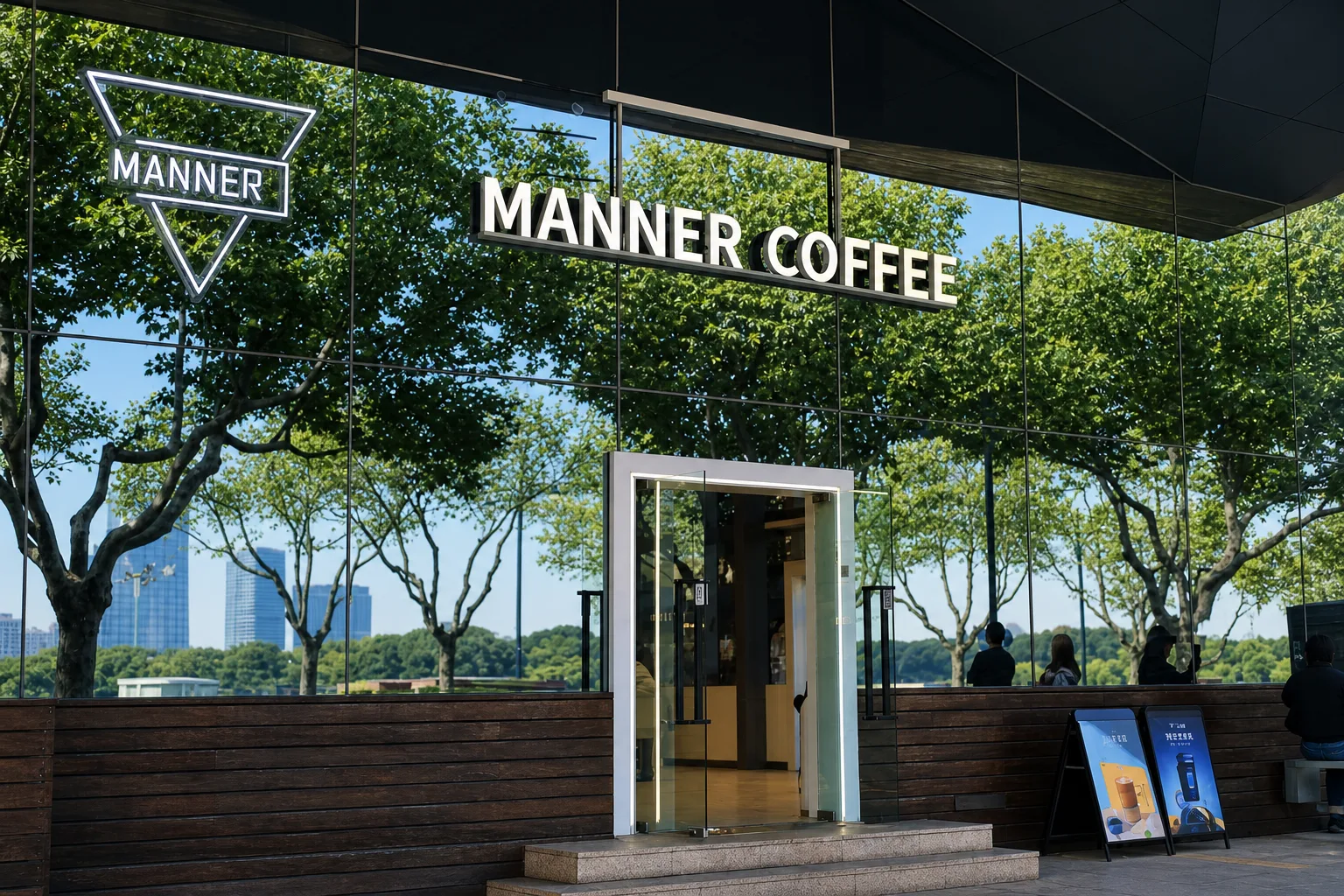 A mirrored MANNER COFFEE storefront reflecting green summer trees